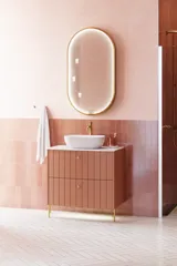Stort vintage badeværelse med terracottafarvet vaskeskab, bordstående håndvask, ovalt spejl med messingkant, lyserøde og grå fliser giver et romantisk, feminint look