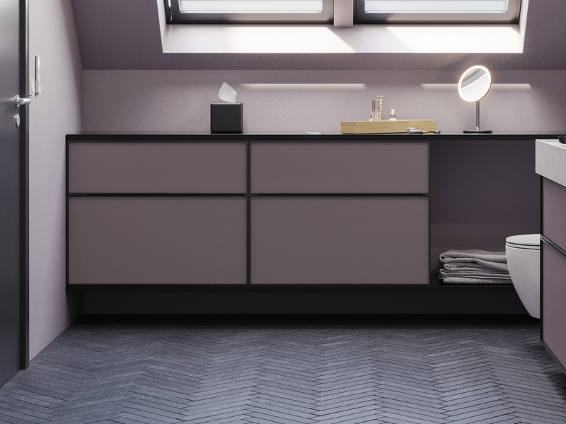 Badeværelse med skrå vægge inspiration, med badeværelsesmøbler i lilla med elegante rammefronter, flot ovalt spejl med lampe, smuk og praktisk hylde, samt lillamalet væg og gråt sildebensgulv, der giver et elegant og moderne udtryk.