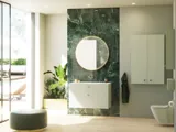Stilfuldt og luksuriøst badeværelse med blide grønne nuancer, et stort elegant rundt spejl og et moderne, sofistikeret grønt toilet