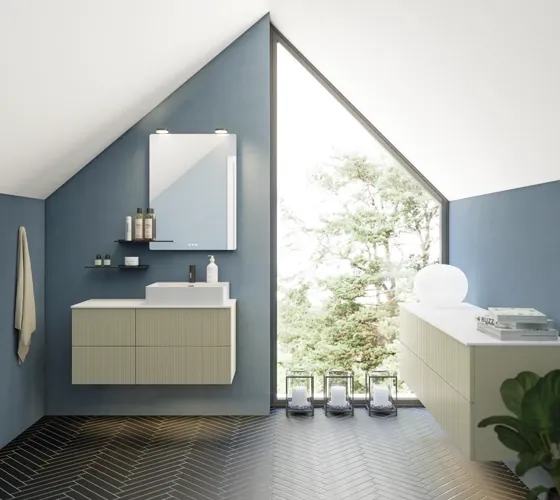 Badeværelse med skrå loft inspiration, beige badeværelsesmøbler med rifler, elegant bordplade samt firkantet bordstående håndvask, smukt firkantet spejl med stilfulde hylder, blå vægge, store vinduer og sort sildebensgulv giver et lyst og urban udtryk.