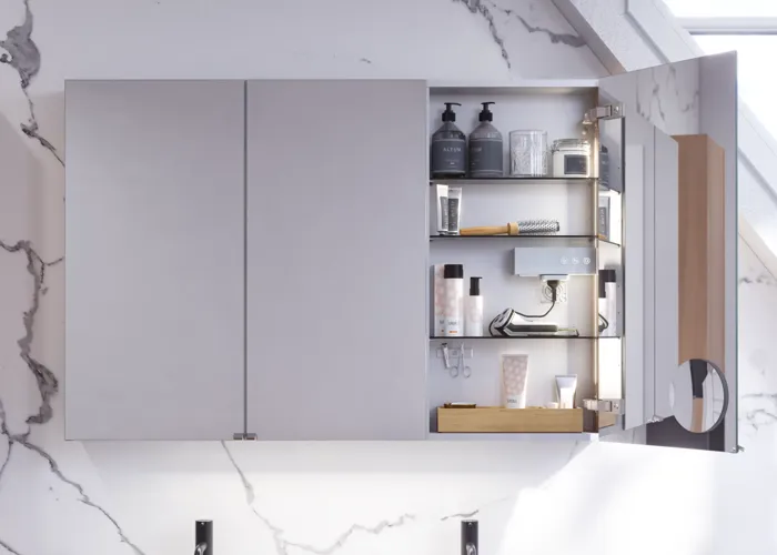 Badeværelse inspiration med vaskeskabe samt overskabe i lys eg med lameller, elegant dobbelt håndvask, smukt spejlskab med lys, sildebensgulv i lys træ og hvid marmorvæg giver et klassisk, lyst og stilrent udtryk.