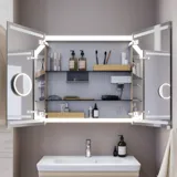 Lille badeværelse inspiration med vaskeskab og overskab over toilet i beige specialfarve, elegant spejlskab med integreret lys, de lyse farver og hvide gardin skaber en romantisk og feminin atmosfære.