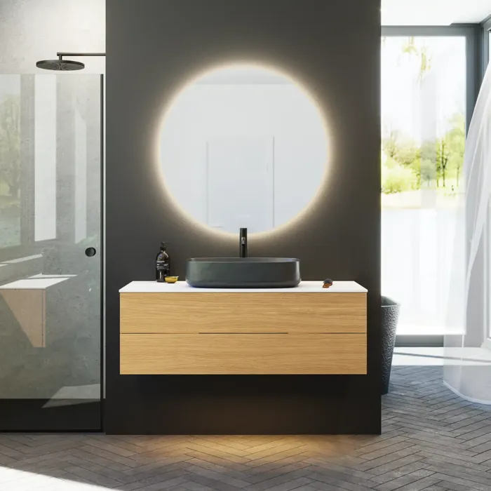 Minimalistisk og stilrent badeværelse inspiration med vaskeskab, underskabe og højskabe i gylden eg, stort rundt spejl med lysstyring, farvet toilet og bordstående håndvask