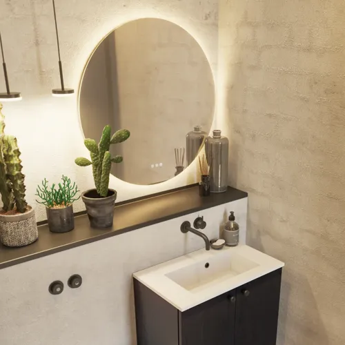 Badeværelse inspiration med vaskeskab i sort eg samt elegant rundt spejl og håndvask, lækkert tilbehør samt kaktusplanter og vægge i rå materialer giver et råt, industrielt og urban look.