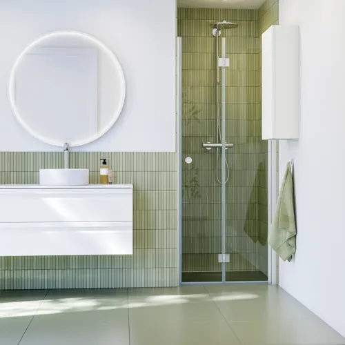 Badeværelse inspiration med hvide badeværelsesmøbler, elegant rundt spejl og bruseniche med foldedør i klart glas og profiler i satin, grønne aflange fliser giver et sofistikeret udtryk.