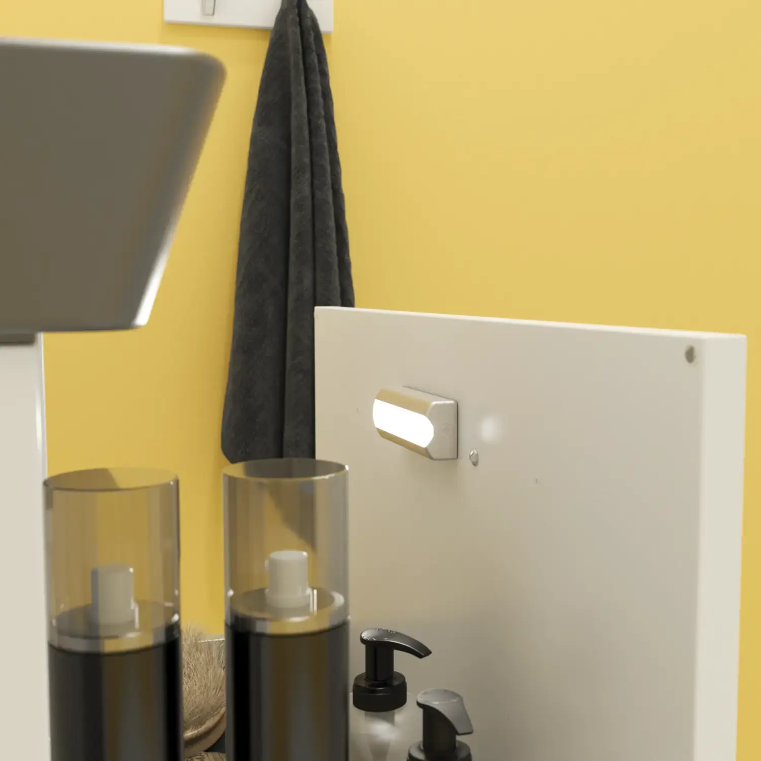 Lille badeværelse inspiration med hvide vaskeskab med sort greb og sort elegant håndvask, smukt rundt spejl med sort kant, forskudt placerede overskabe samt terrazzo væg og gulv samt gule væge giver et modigt og moderne look.