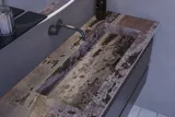 Stort badeværelse inspiration med grå vaskeskab med integreret greb, stilfuld sidestillet håndvask, firkantet spejl med afrundede hjørner, vægge i beton look samt rå materialer giver et urban udtryk